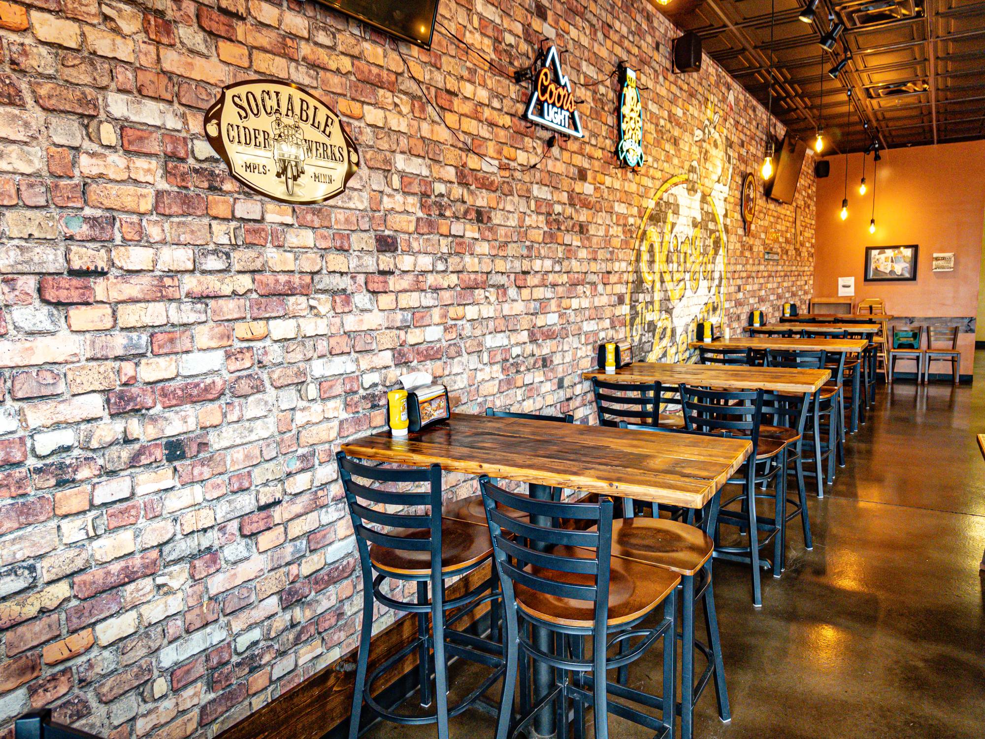 Back corner view of dining area with clean flooring, spaced seating, and light streaming through windows.